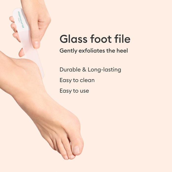 A hand uses the Manucurist-us Glass Foot File on a bare heel. Text: Gently exfoliates for soft, smooth skin. Durable, long-lasting, easy to clean and use.