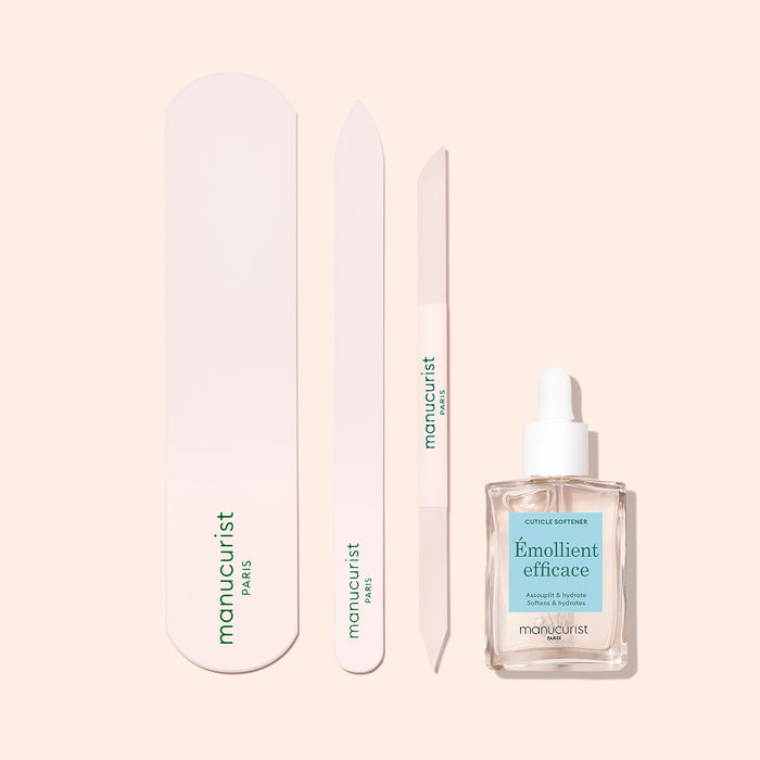 The Manucurist-us Glass Foot File set includes a nail file, buffer, cuticle pusher, and Émollient efficace dropper bottle, all displayed on a light beige background. Ideal for exfoliating heels and achieving smooth skin.
