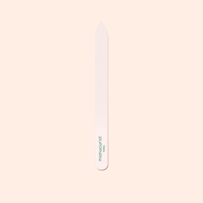 The Manucurist-us Glass Nail File features a pointed tip and "manucurist" in green near the base, shown vertically on a pale beige background.