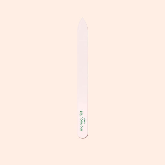 The Manucurist-us Glass Nail File features a pointed tip and "manucurist" in green near the base, shown vertically on a pale beige background.