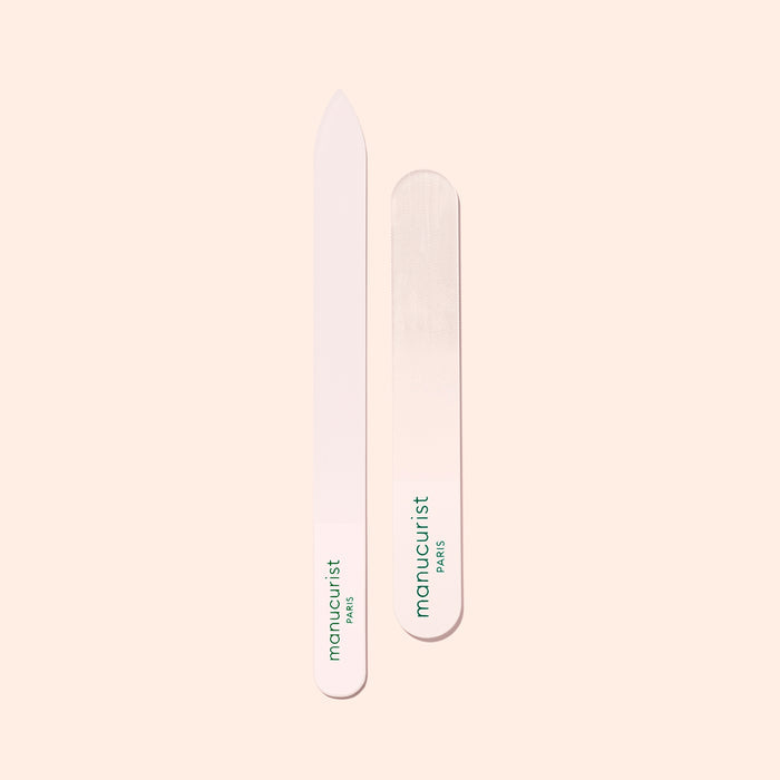 Two Manucurist-us Glass Nail Files, each with green "manucurist PARIS" text, are shown vertically on a light beige background. One file features a pointed end while the other has a rounded end.