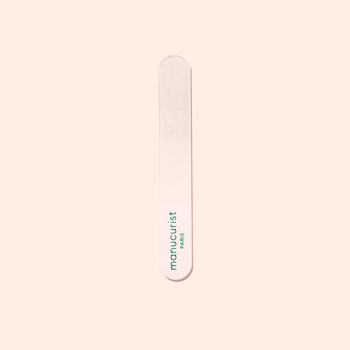 A Manucurist-us Glass Polisher with rounded ends rests on a pale surface. “Manucurist-us” is printed vertically in green, making it ideal for gently enhancing the natural shine of your nail plate.