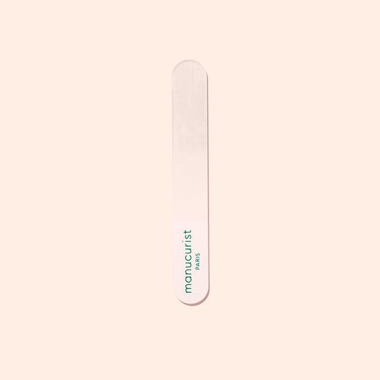 A Manucurist-us Glass Polisher with rounded ends rests on a pale surface. “Manucurist-us” is printed vertically in green, making it ideal for gently enhancing the natural shine of your nail plate.