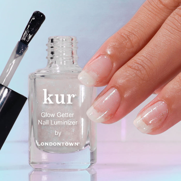 A hand with glossy, shimmery nails is shown next to an open bottle of Glow Getter Nail Luminizer - Diamanté by LONDONTOWN, delivering luminous care and an ethereal finish.