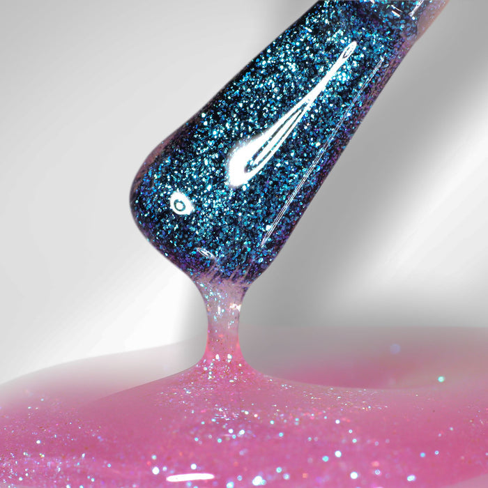 Close-up of a brush applying LONDONTOWN Glow Getter Nail Luminizer - Prism, a sparkly blue polish on a shiny pink surface, creating an ethereal finish with 360° care for your nails.
