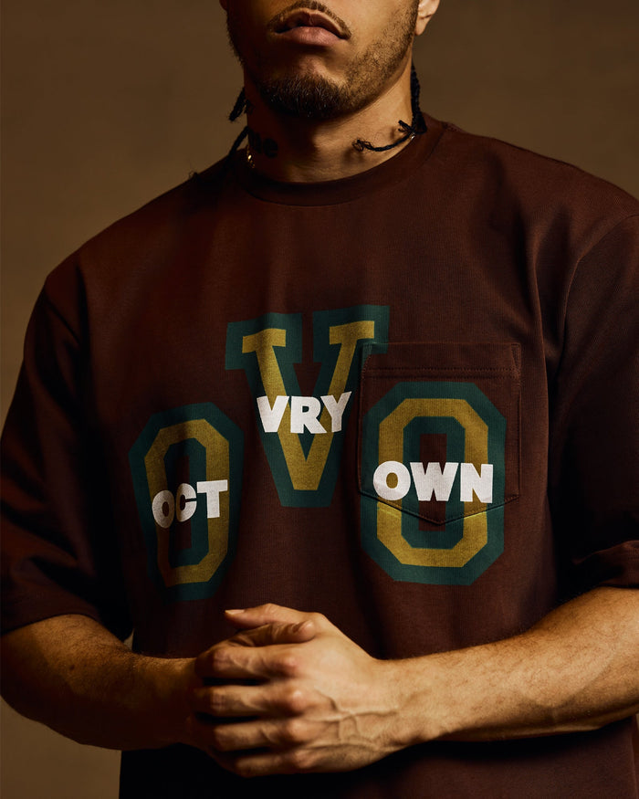 Brown heavy jersey pocket tee with green and gold graphic text and chest pocket.