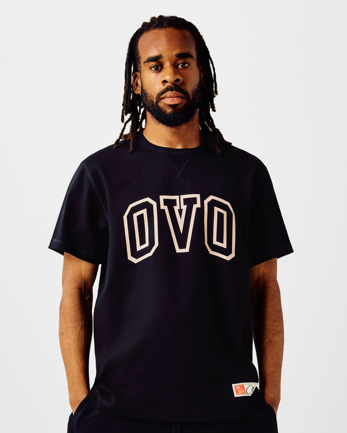Man wearing dark navy short-sleeve t-shirt with cream-colored "OVO" graphic print on chest.