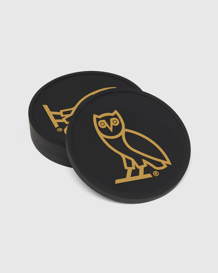 Four black round coasters with gold owl and lightning bolt icons.