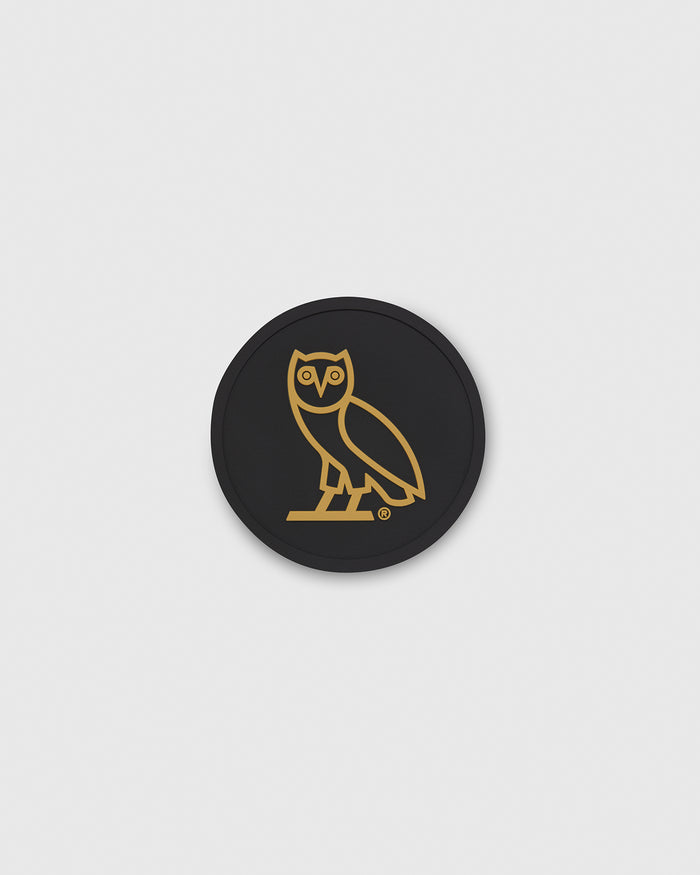Black circular coaster with gold owl icon outline in center.