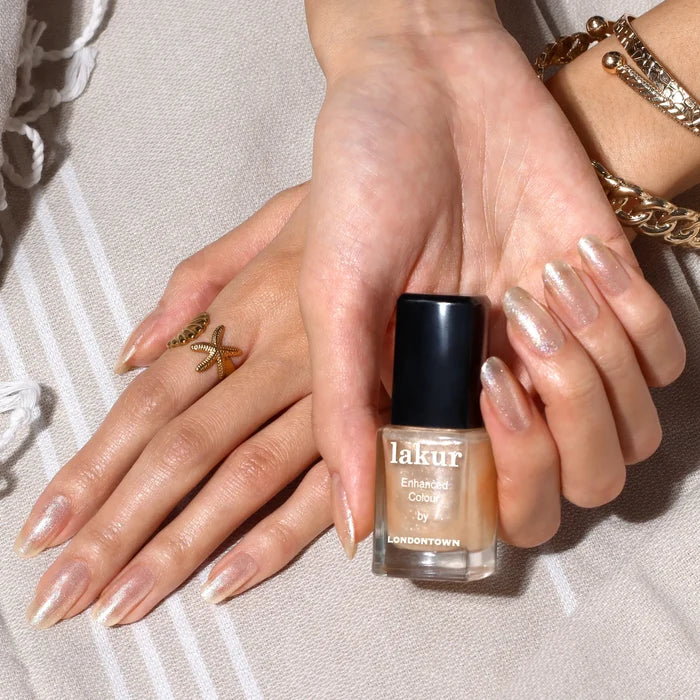 A person's hands with pearlescent nail polish, a gold starfish ring, and gold bracelets are shown holding a bottle of LONDONTOWN's Isla Bonita nail polish.