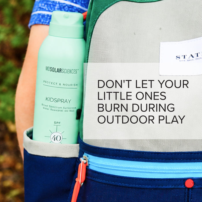 A mint green bottle of MDSolarSciences KidSpray sunscreen tucked into a navy blue backpack pocket, with a white text overlay that reads 'DON'T LET YOUR LITTLE ONES BURN DURING OUTDOOR PLAY'.