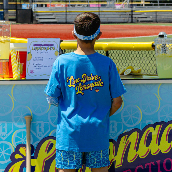 Youth model wearing blue youth graphic tee with "Lemonade" design