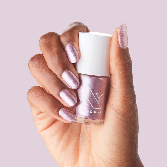 Hand holding Lilac Shimmer nail polish bottle with nails painted in soft metallic purple for a polished mani look