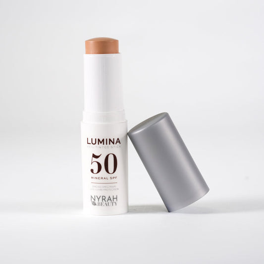 A white stick sunscreen bottle labeled 'LUMINA 50 MINERAL SPF' with a silver cap leaning beside it on a light gray background.