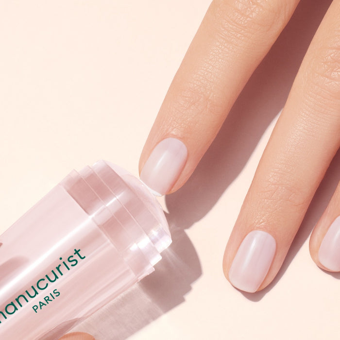 A hand with neat, natural nails applies the transparent Manucurist US Mani stamper stick, ideal for flawless French tips or a smooth base before stamping, all against a light background.