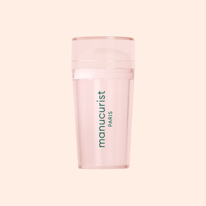 A translucent pink Mani stamper by Manucurist US, ideal for French tips, features "manucurist PARIS" in vertical green print on the front and is displayed against a pale peach background.