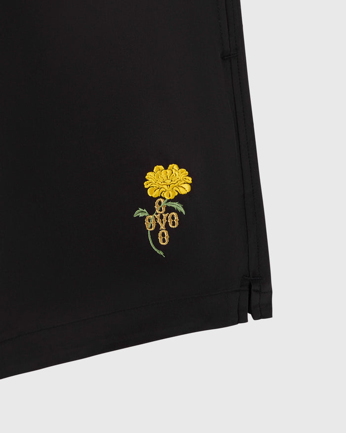 Black swim short with yellow marigold flower embroidery and green leaf detail on leg.