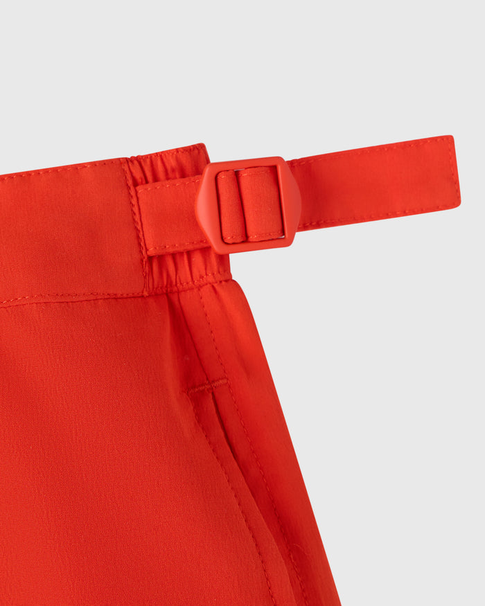 Signal orange swim short with elasticated waistband and red plastic buckle detail at side.