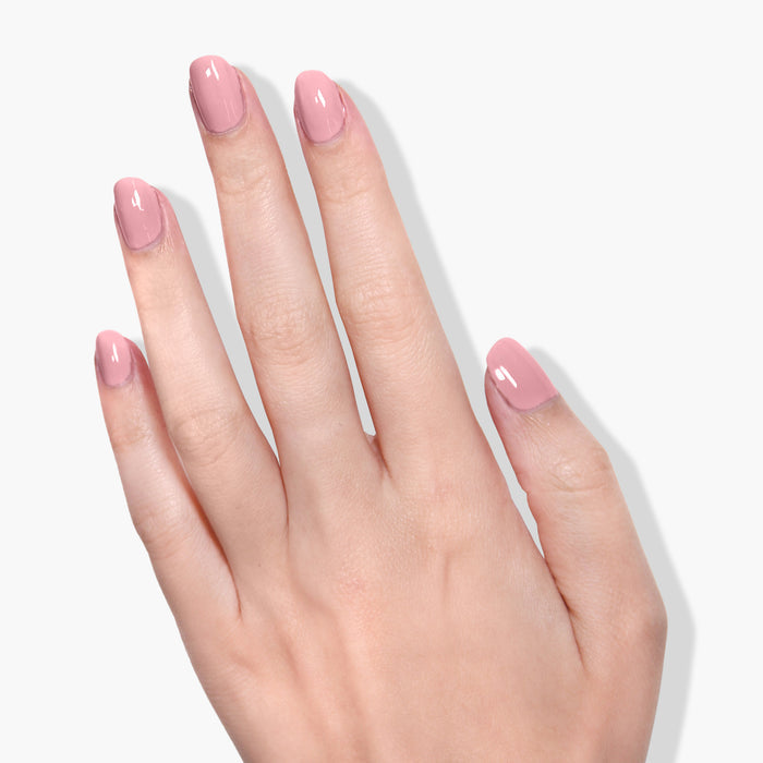 A hand with light pink, glossy manicured nails polished with LONDONTOWN's "Mauve Over" soft crème nail polish is shown against a plain white background.