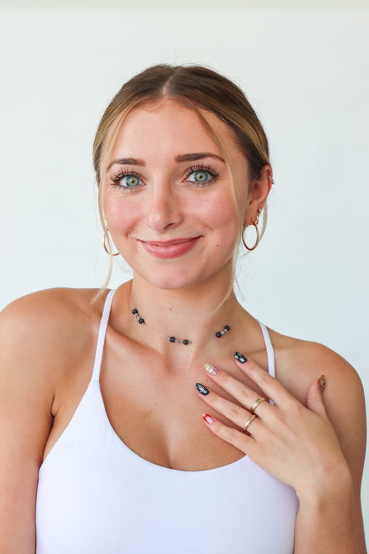 Woman wearing necklaces and a ring, smiling against a white background