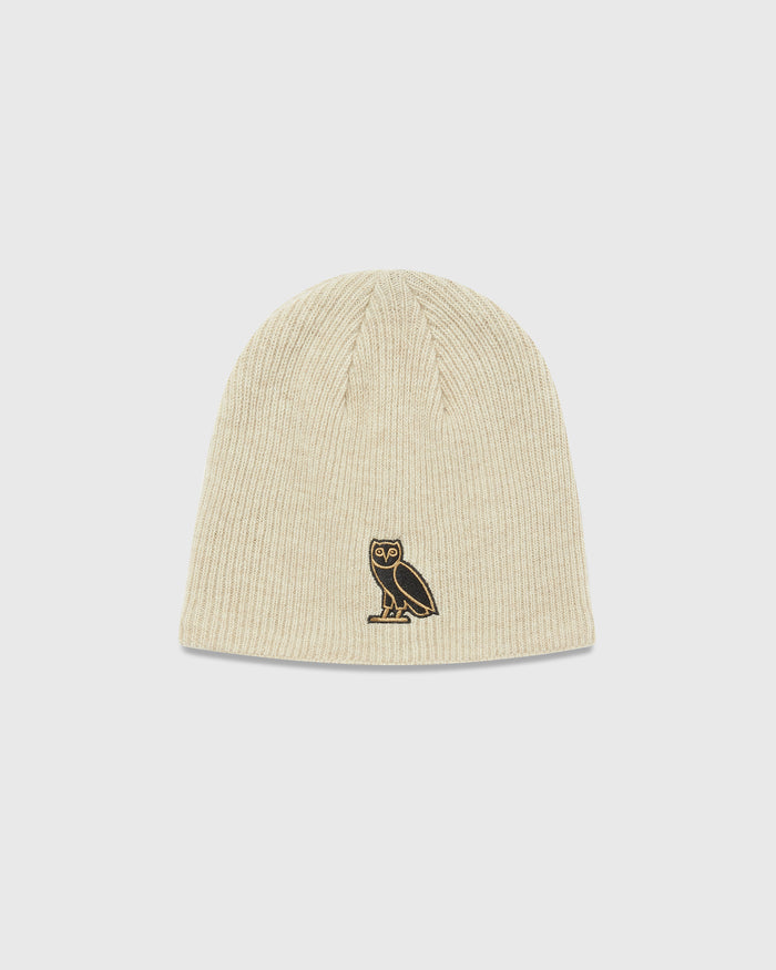 Sand-colored ribbed beanie with embroidered owl logo on front.