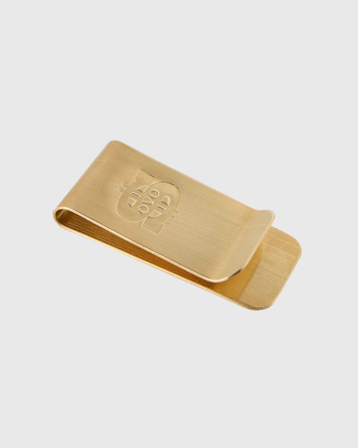 Gold-toned money clip with engraved logo on front and curved spring clip on back.