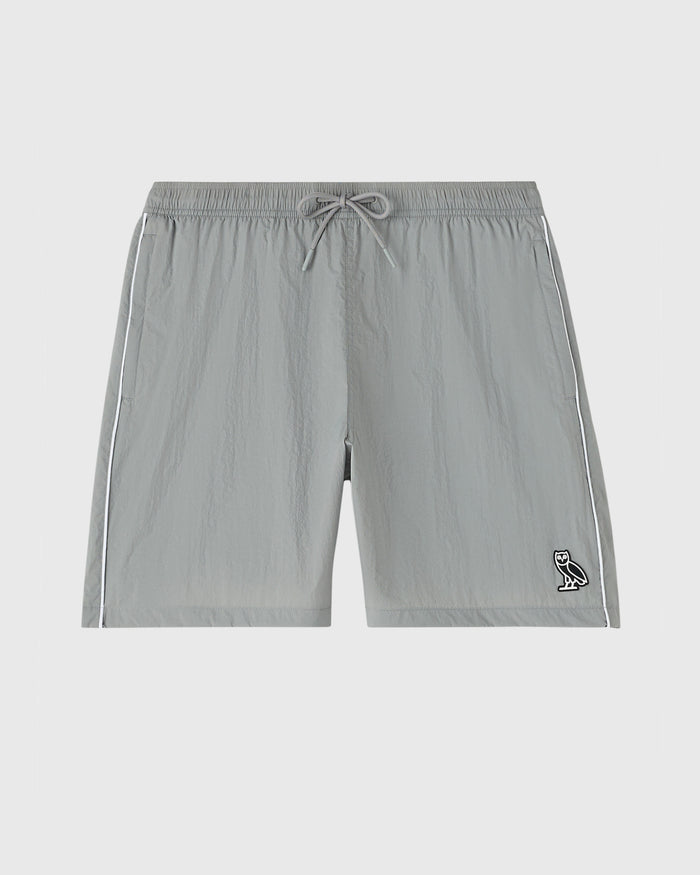 Cool grey nylon track shorts with drawstring waist, side stripes, and small owl logo on lower right leg.