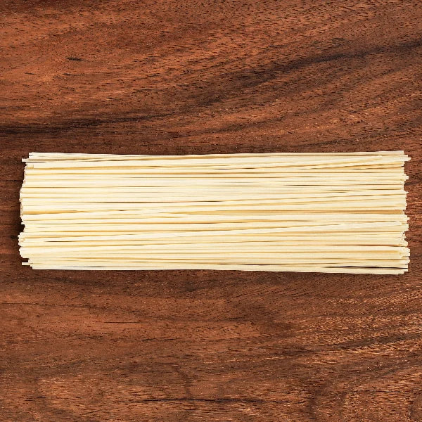 A bundle of flat, pale yellow dried pasta noodles laid horizontally on a dark brown wooden surface.