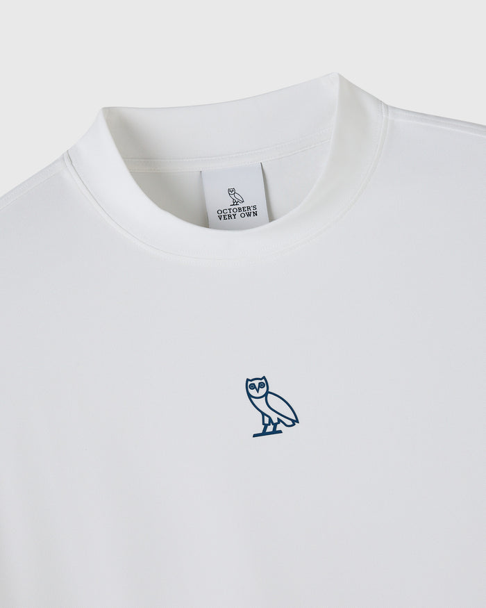 White mockneck tee with small blue owl embroidered on chest and OVO label visible at neckline.