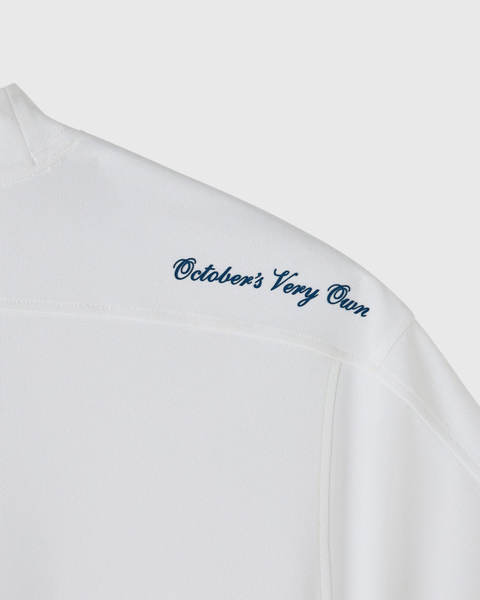 White mockneck tee with "October's Very Own" embroidered in blue script across the chest.