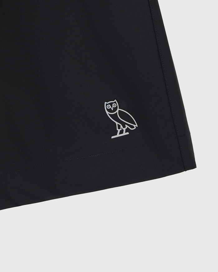 Black stretch nylon golf short with white owl logo embroidered on thigh.