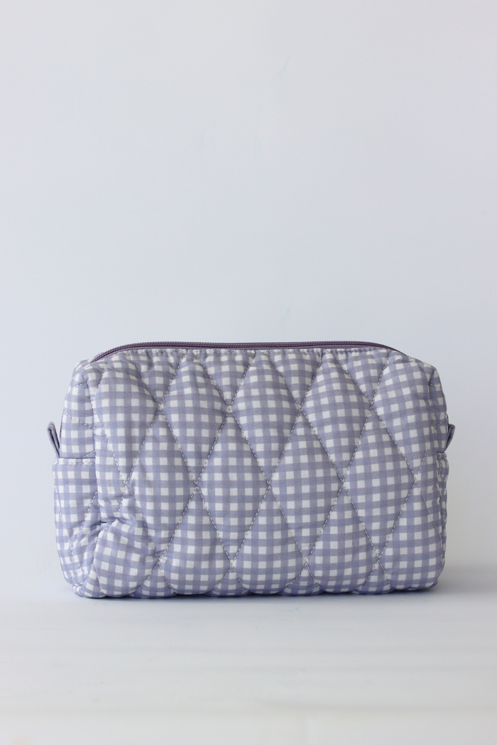 A quilted cosmetic pouch with a light blue and white gingham pattern, featuring a diamond-quilted texture and a dark purple zipper, set against a plain light gray background.
