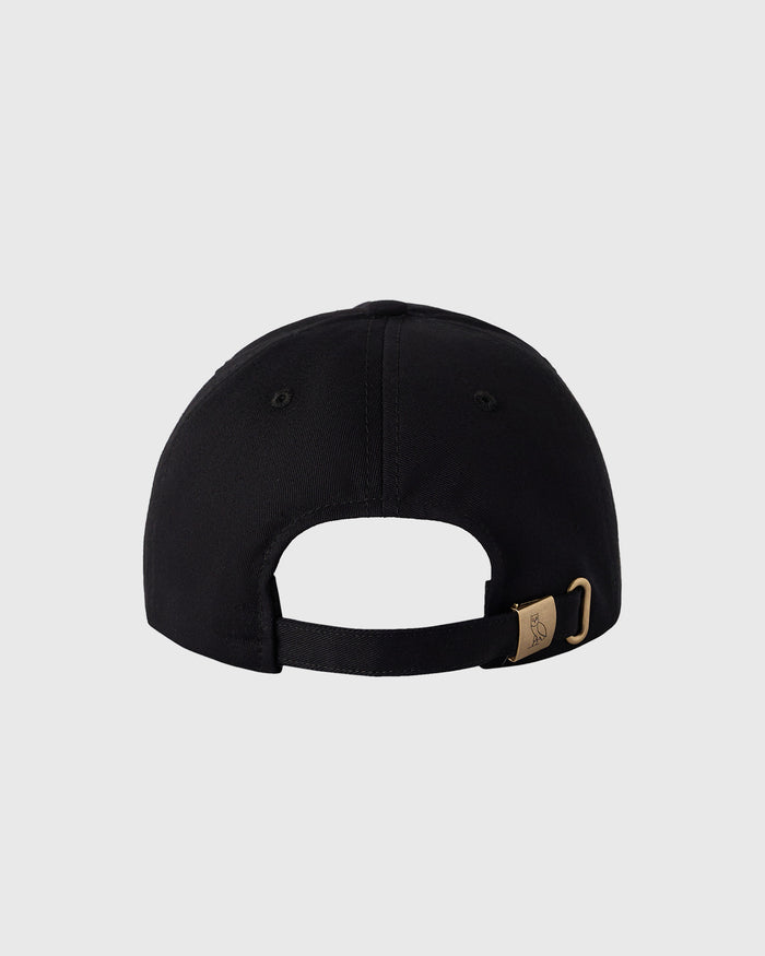 Black baseball cap with pom pom on crown and adjustable back closure with metal buckle.