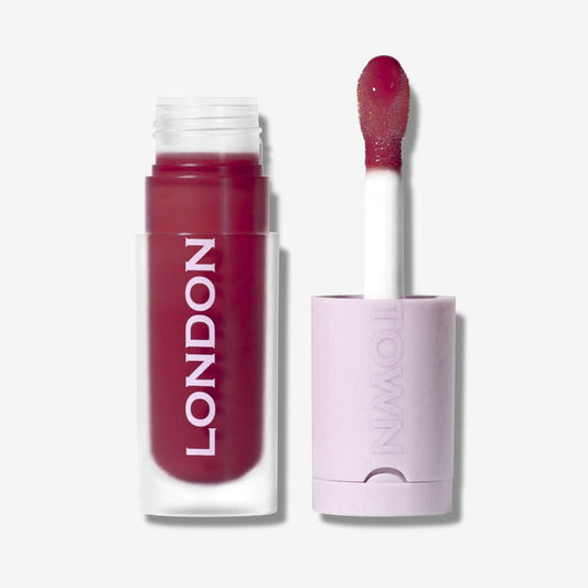 A tube of LONDONTOWN Quench Glow Buttery Lip Oil in "Berry Glaze," giving a plush shine, is shown with its applicator wand beside it against a light background.