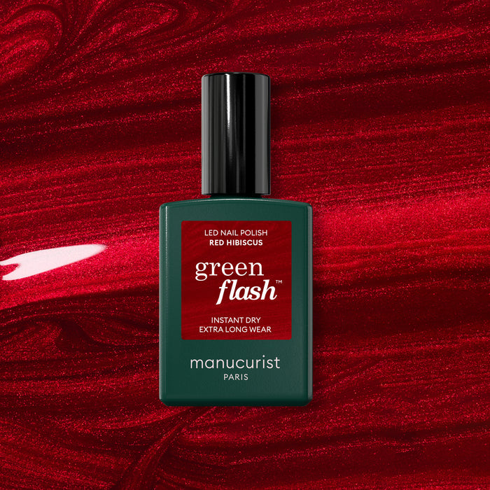 A bottle of Manucurist Red Hibiscus gel polish rests on a vibrant, glossy red background.