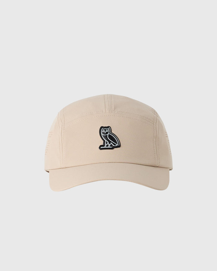 Sandstone five-panel cap with small black owl emblem on front.