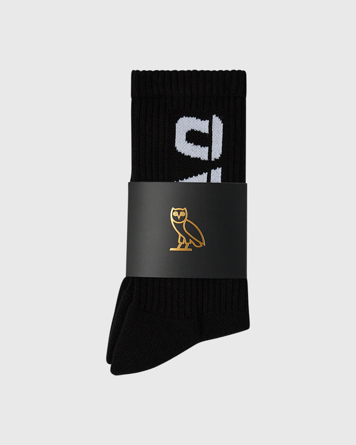Black ribbed crew socks with white logo design on cuff, wrapped in branded band.