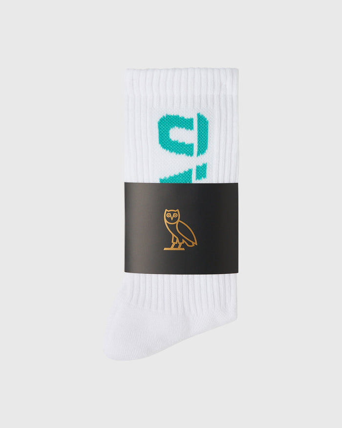 White ribbed crew socks with teal graphic design, rolled and banded with black label featuring gold owl logo.