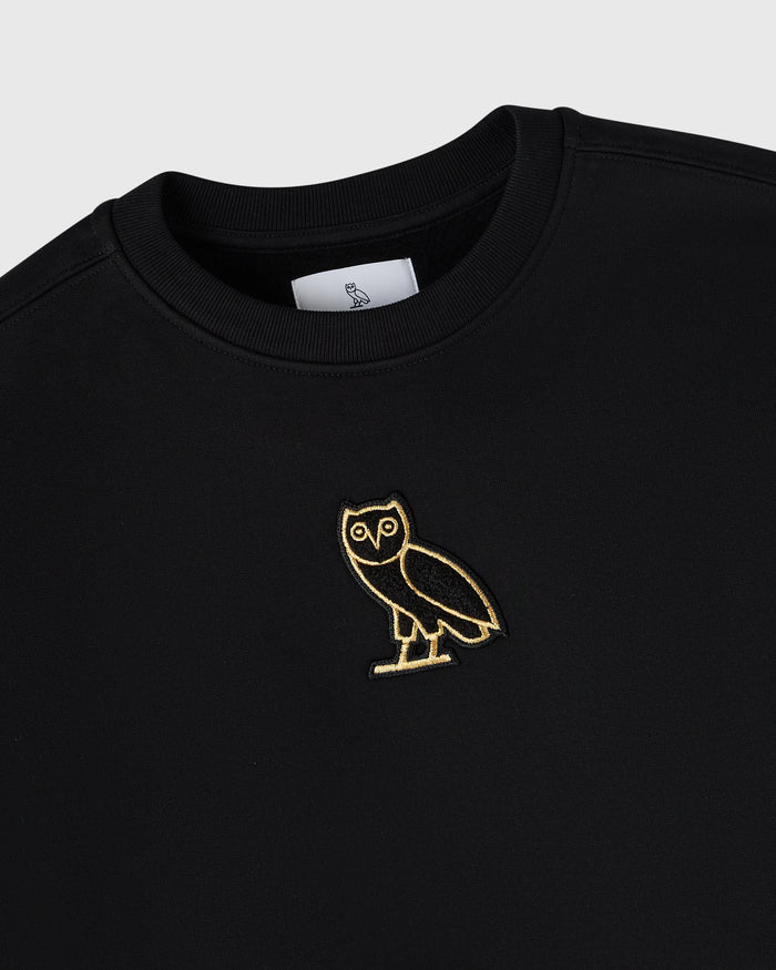 Black crewneck sweatshirt with gold owl embroidery on chest and brand label at neckline.
