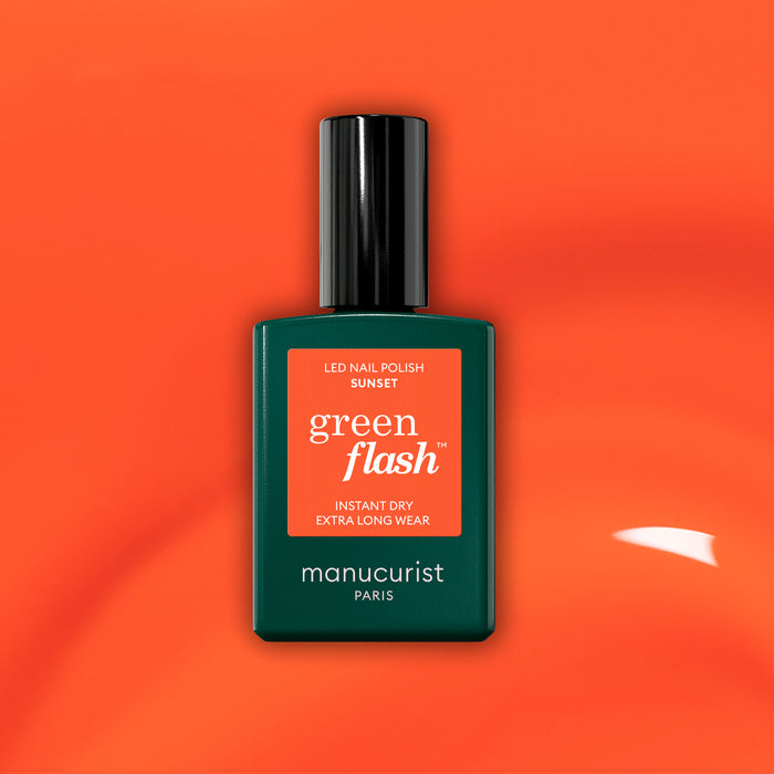 A bottle of Manucurist Sunset gel polish, featuring a dark green label and black cap, is displayed against a vibrant orange background.