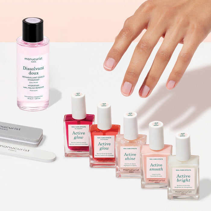 A manicured hand hovers above the Manucurist Super Active Manicure Kit, which includes five bottles of nail polish, nail polish remover, and two nail files—all beautifully arranged on a white surface for a flawless at-home manicure.