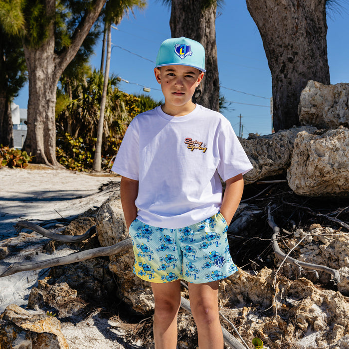 Person wearing a white t-shirt with 'Swing into Spring' text and floral shorts standing outdoors with rocks and trees in the background
