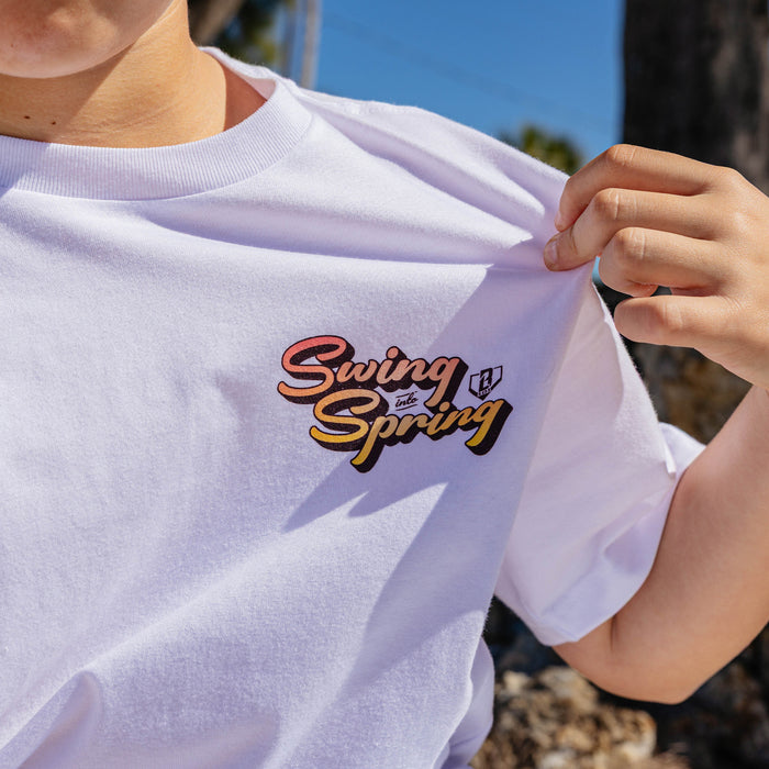 White t-shirt with 'Swing into Spring' text held by a person outdoors.