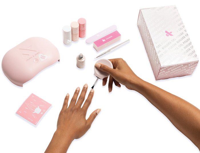 The Gel Mani System + Builder Gel Kit - 6 showing a hand applying gel polish with lamp, nail care tools, and packaging visible