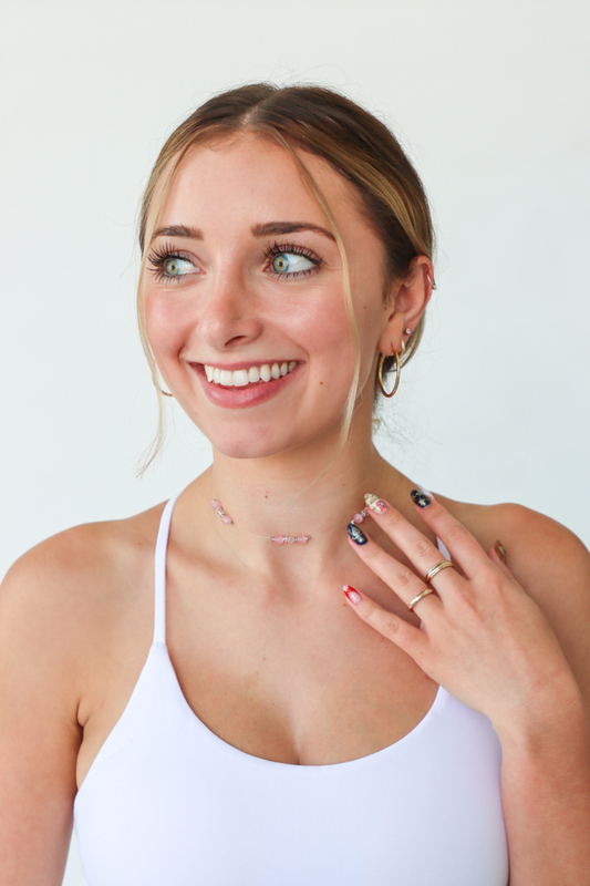 Woman wearing a white tank top with visible jewelry against a plain background