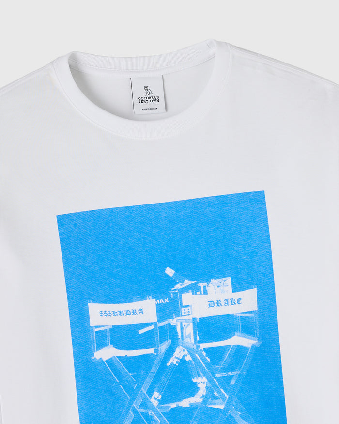 White long-sleeve tee with blue graphic print featuring director's chairs and text on chest.