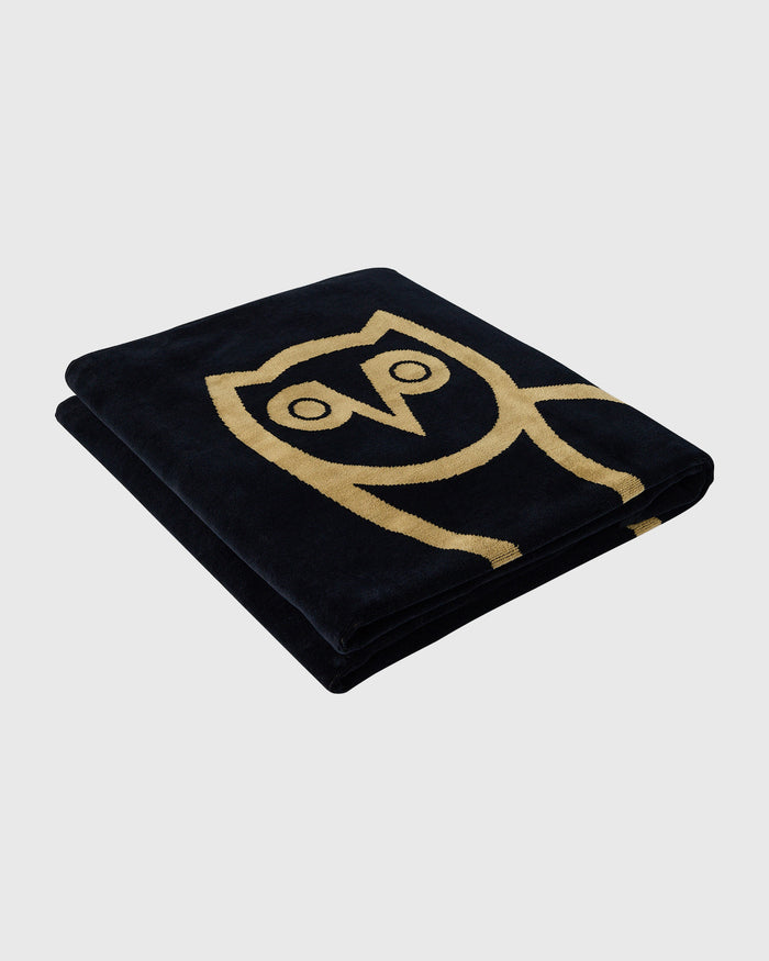 Black towel with gold owl face design embroidered on front.