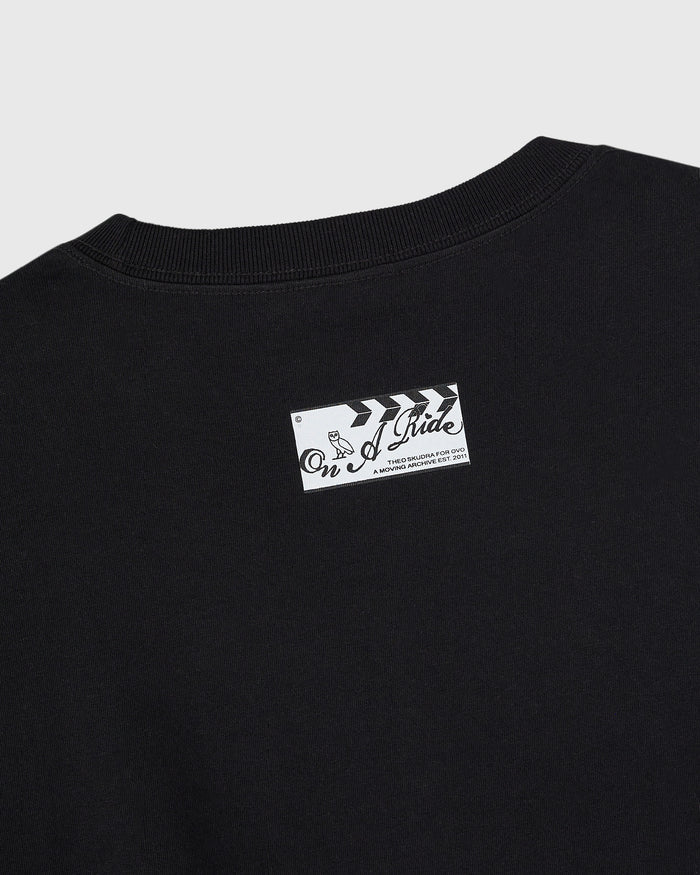 Black crewneck t-shirt with white graphic label on chest featuring "On A Ride" text and arrow design.