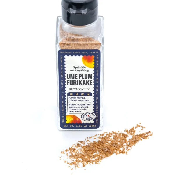 A clear plastic bottle of Ume Plum Furikake seasoning with a black cap and a blue label, shown on a white background with a small pile of the brown seasoning spilled in front.