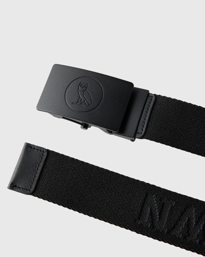 Black webbed belt with owl emblem on metal buckle and leather end tab.